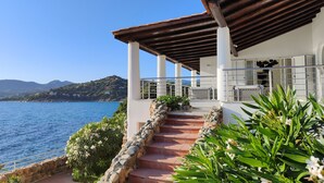 A coastal building with a stone staircase leading to a covered terrace overlooking the sea.