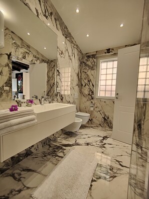 Une salle de bain avec des murs et un sol en marbre, un grand miroir, un lavabo avec une serviette et des toilettes.