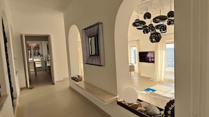 A hallway with a view into a living area featuring a television, a decorative mirror, and a unique spherical light fixture.