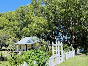 Een huis met een blauw dak, omgeven door weelderig groen en een witte hekken.