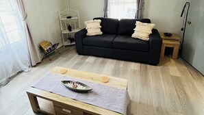 Una sala de estar con un sofá negro, una mesa de centro de madera y una estantería blanca.