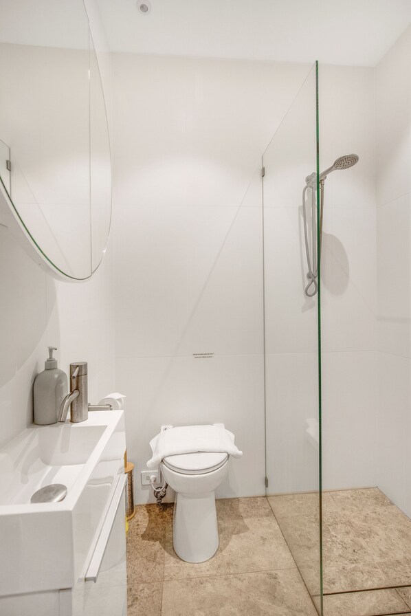 Un baño moderno con cabina de ducha de vidrio, inodoro blanco y tocador con espejo.