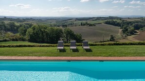 Una piscina con tre lettini che si affacciano su un panorama suggestivo di colline e alberi.