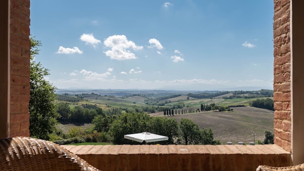 Un tavolo in vimini apparecchiato con una brocca, bicchieri e un teiera, con vista su un paesaggio suggestivo attraverso una finestra ad arco.