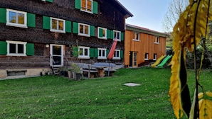 A multi-story building with green shutters, a wooden exterior, and a grassy yard with a slide. - Quaint farmhouse in the countryside with its own garden, 10 beds (Weitnau)