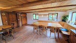 A rustic wooden interior with a large dining table, wooden chairs, and a bench. There are two windows with plants on the windowsill. - Quaint farmhouse in the countryside with its own garden, 10 beds (Weitnau)
