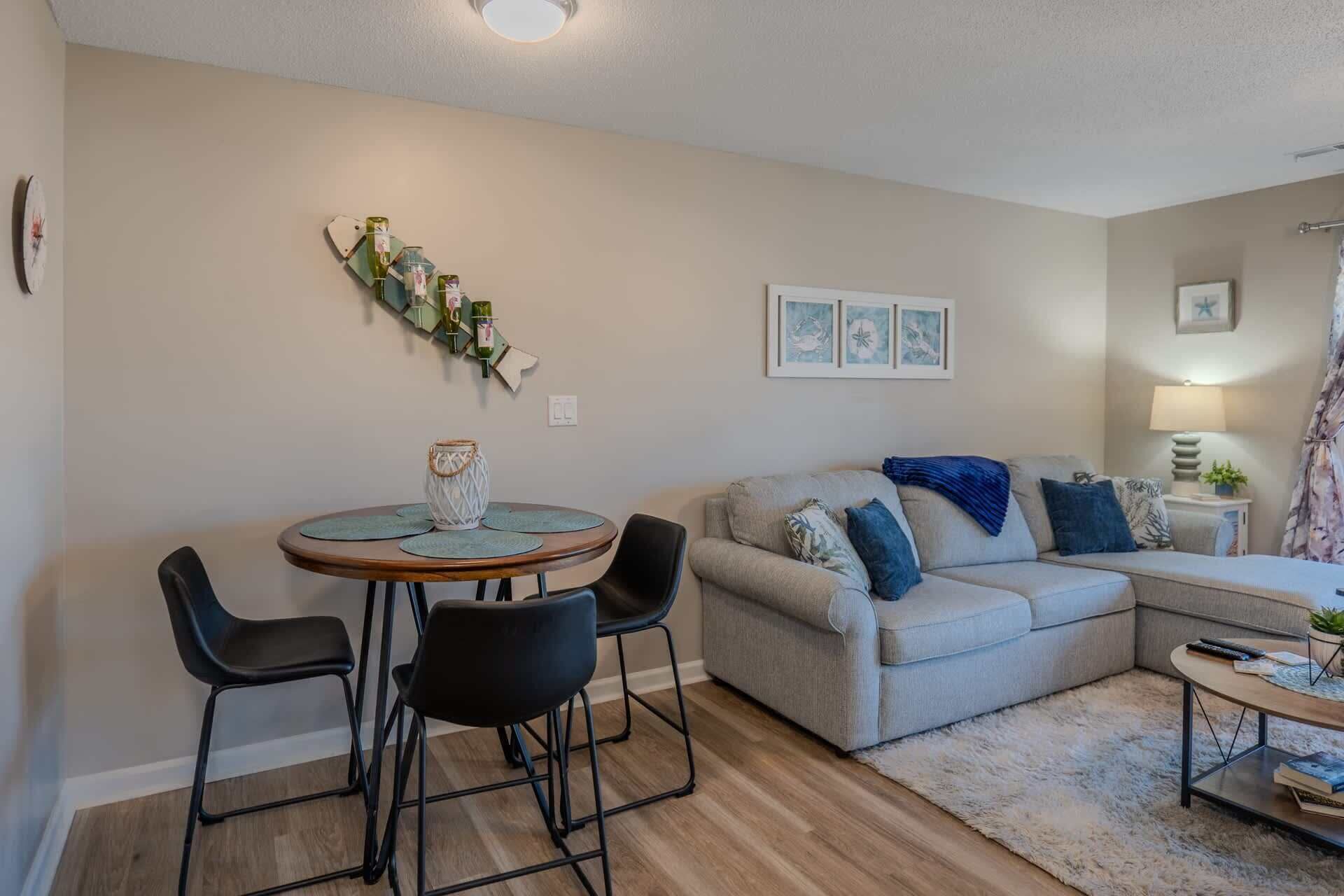 Een woonkamer met een bank, twee stoelen, een ronde tafel met een decoratieve vaas, wanddecoratie en een lamp.