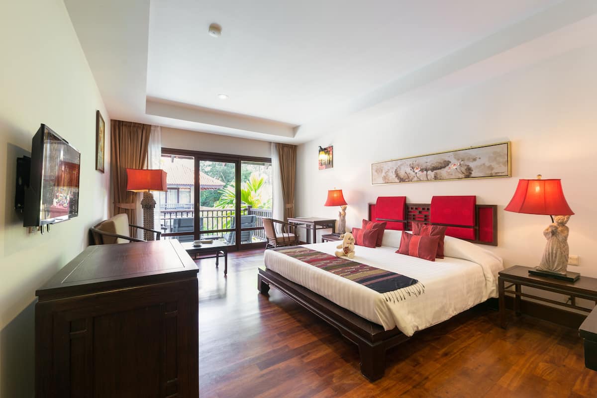 Quarto de hotel com uma cama grande, uma mesa, uma cadeira e uma varanda com vista para o verde.