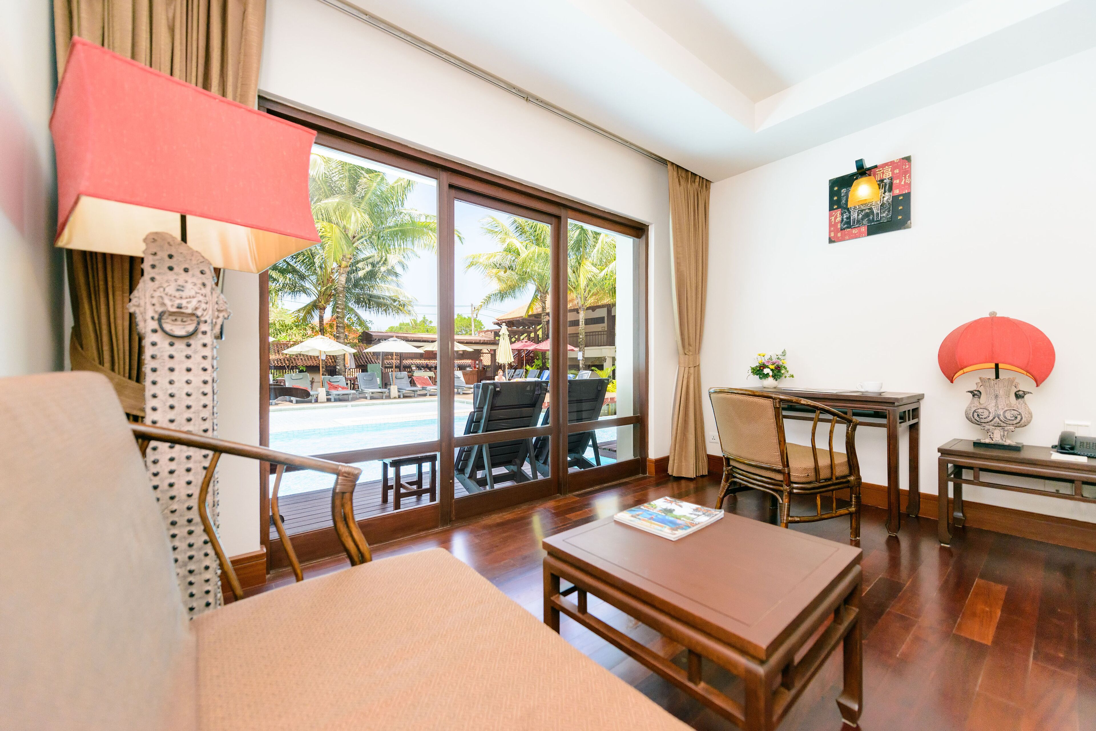 A hotel room with a large window, wooden furniture, and a view of an outdoor pool area.