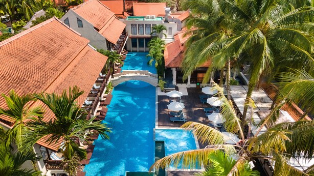 A long swimming pool with a clear blue water, surrounded by palm trees and buildings with red-tiled roofs. - Khaolak Oriental Resort - Adult Only (Takua Pa)