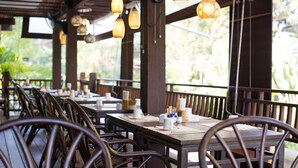 A restaurant with wooden tables and chairs, hanging pendant lights, and a view of greenery outside. - Khaolak Oriental Resort - Adult Only (Takua Pa)