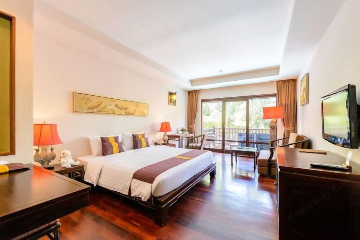 Ein Hotelzimmer mit einem großen Bett, einem Schreibtisch, einem Stuhl, einem Fernseher und einem Balkon mit Vorhängen.