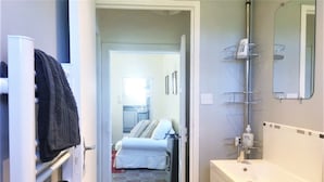 Et badeværelse med en hvid vask, et spejl og et bruseområde med en metalhylde.