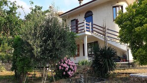 A two-story house with a balcony, surrounded by various trees and plants. - Vesime Villa with Garden (Vesime (AT))