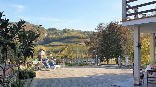 A courtyard with a stone pathway, lounge chairs, and a view of rolling hills. - Vesime Villa with Garden (Vesime (AT))