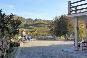 A courtyard with a stone pathway, lounge chairs, and a view of rolling hills. - Vesime Villa with Garden (Vesime (AT))