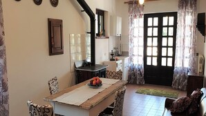 A dining area with a wooden table and patterned chairs, a kitchen with a stove, and a large window with curtains. - Vesime Villa with Garden (Vesime (AT))