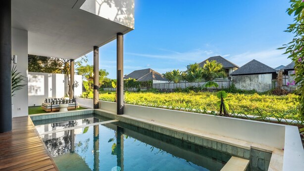 Ein moderner Poolbereich im Freien mit Holzterrasse, einer Lounge mit Kissen und Blick auf angrenzende Häuser.