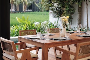 A wooden dining table set for six with chairs, surrounded by lush greenery and a view of a garden.