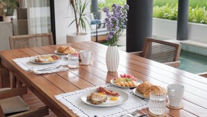 Ein Holztisch mit Frühstücksleckereien, eine Vase mit Blumen und Blick auf einen Garten.