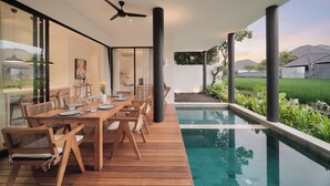 Ein moderner Essbereich im Freien mit Pool, Holzmöbeln und Deckenventilator.