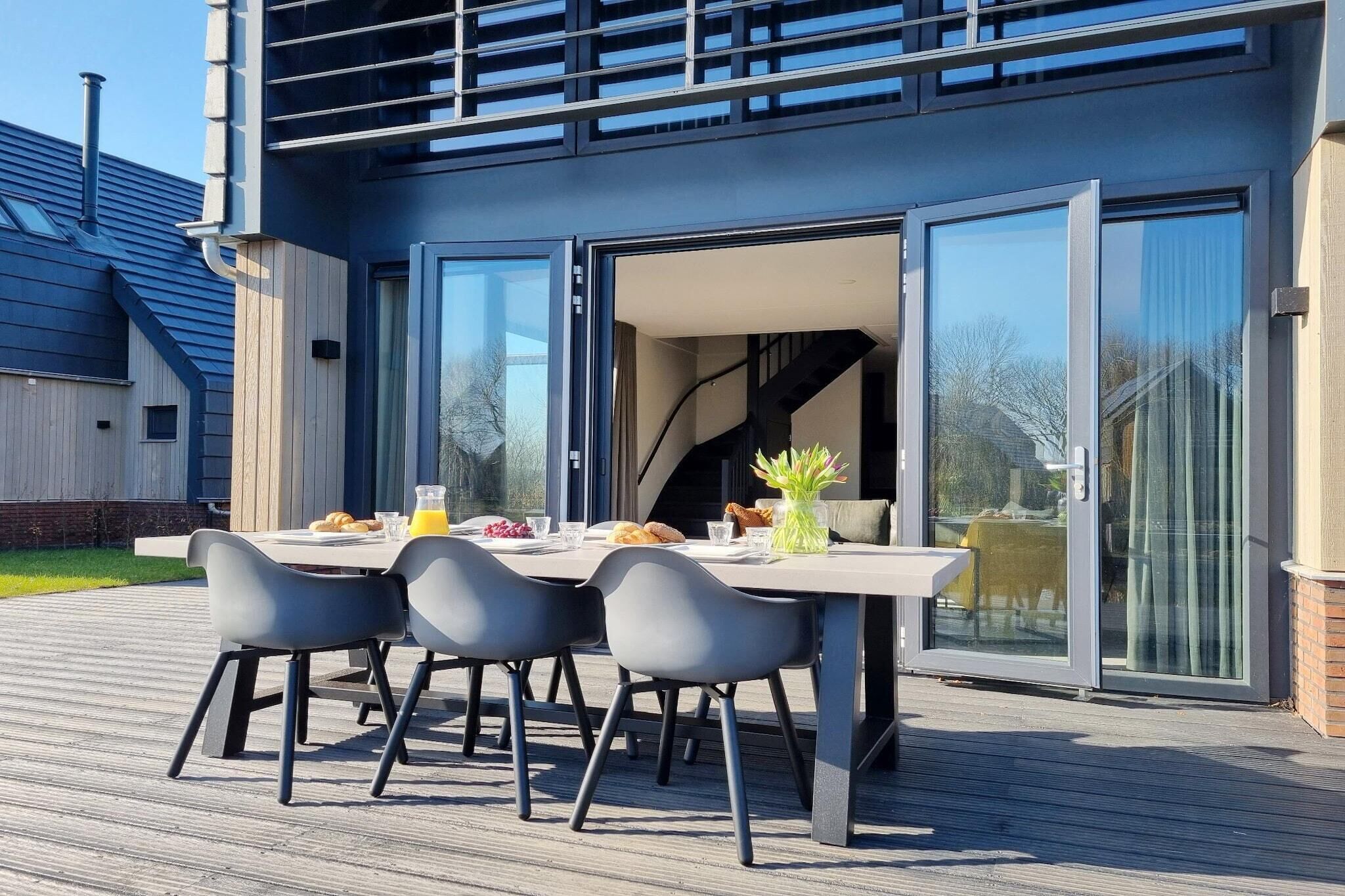 Ein Essbereich im Freien mit Tisch und Stühlen, eine Glastür zu einem Innenraum sowie eine Holzterrasse.