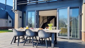 An outdoor dining area with a table and chairs, a glass door leading to an interior space, and a wooden deck. - Water Villa in Balk by Frisian Lakes (Balk)