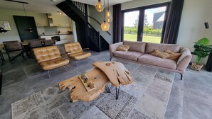 Ein modernes Wohnzimmer mit Ledersofas, einem Holztisch und einer Treppe, die in eine Küche führt.