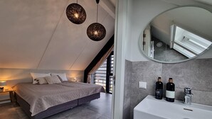 Ein modernes Schlafzimmer mit einem großen Bett, einem runden Spiegel und einem weißen Waschbecken mit Flaschen.