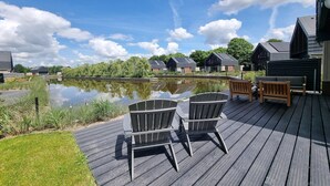 A deck with Adirondack chairs overlooking a calm water body, surrounded by modern buildings with sloped roofs. - Waterfront Villa w/ Jetty (Balk)