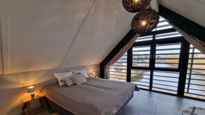 A bedroom with a large bed, a nightstand with a lamp, and a view through a large window. - Waterfront Villa w/ Jetty (Balk)