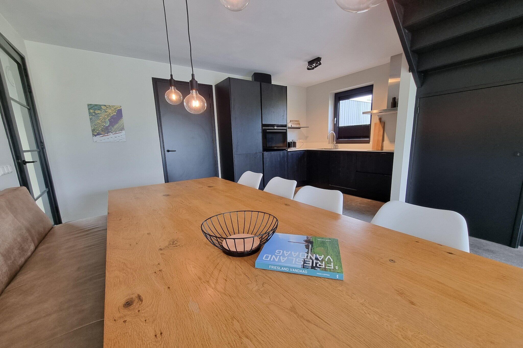 A modern dining area with a wooden table, white chairs, a black metal bowl, and a book titled "Friesland Vantaa".