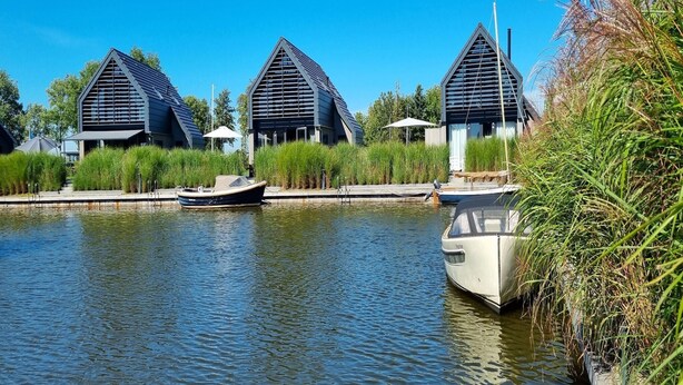 Un bâtiment moderne doté d’un toit triangulaire, avec un plan d’eau au premier plan et un bateau amarré à proximité.