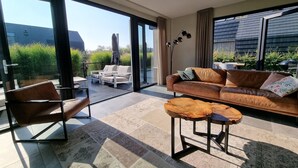 Un salon moderne comprenant un canapé, un fauteuil, une table basse et un lampadaire. Une porte-fenêtre coulissante donne accès à un espace extérieur avec une table et des chaises de patio.