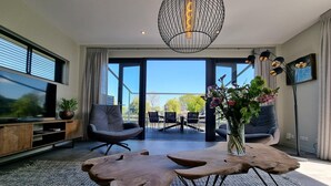 Una sala de estar moderna con una mesa de centro de madera, un sofá gris, un televisor sobre un mueble de madera y un ventanal con vistas al exterior.