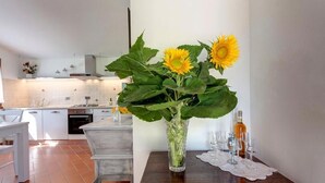 A kitchen with white cabinets, a dining table with a vase of sunflowers, and wine glasses. - Casa de' Fossi (Reggello)