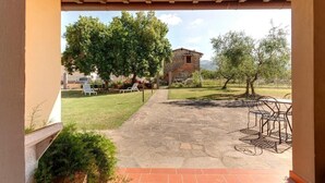 A patio with stone flooring, outdoor seating, and a view of a stone building and trees. - Casa de' Fossi (Reggello)