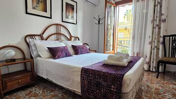 Un dormitorio ordenado con cama, mesita de noche, silla y ventana con cortinas.