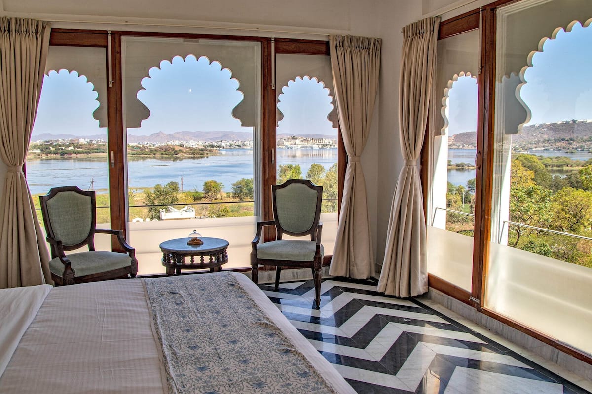 A room with a bed, two chairs, a small table, and large windows with decorative cutouts.