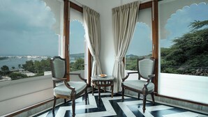 A balcony with two chairs, a small table, and a view of a body of water and greenery. - Burj Baneria - A Boutique Homestay (Udaipur)