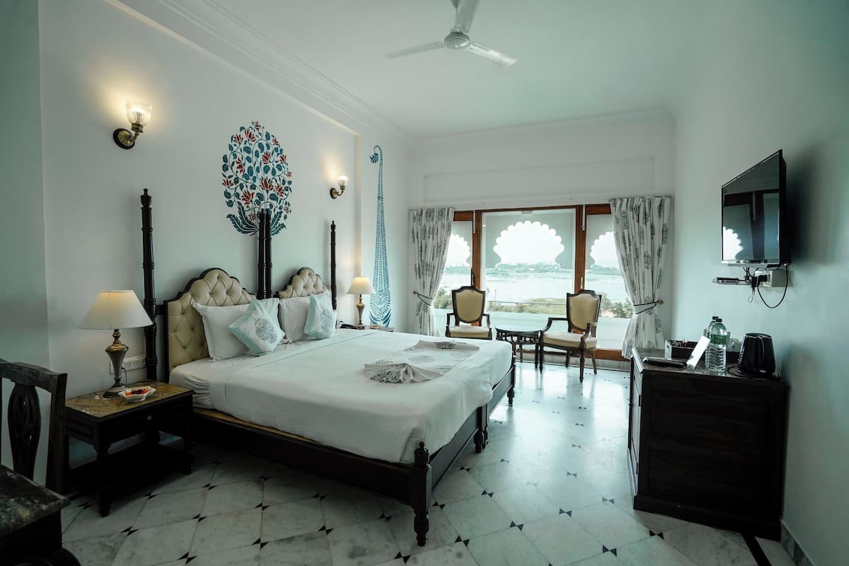 A hotel room with a bed, bedside tables, a desk, a chair, a television, and a view of the sea.