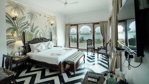 A hotel room with a large bed, a desk, a chair, a TV, and a view of the outdoors. - Burj Baneria - A Boutique Homestay (Udaipur)