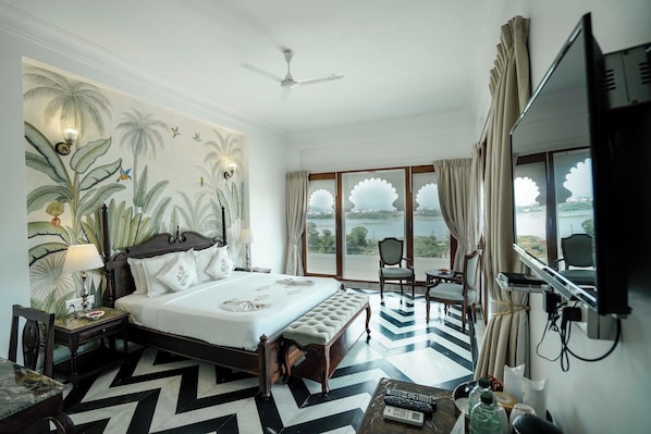 A hotel room with a large bed, a desk, a chair, a TV, and a view of the outdoors.