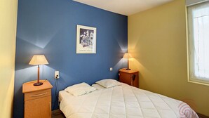 Een slaapkamer met een bed, twee nachtkastjes met lampen, een klein houten kastje en een aan de muur hangend schilderij.