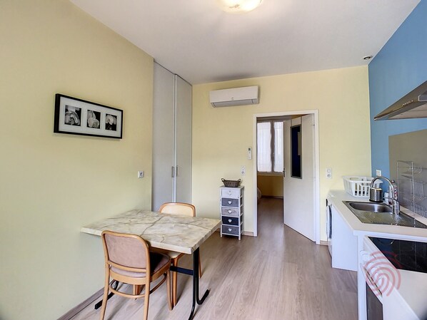A compact kitchen with a dining area, featuring a table, chairs, a small cabinet, and an air conditioning unit.