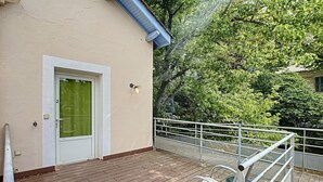 Een balkon met een metalen hekwerk, een deur met een groen gordijn en een vloer van baksteen.