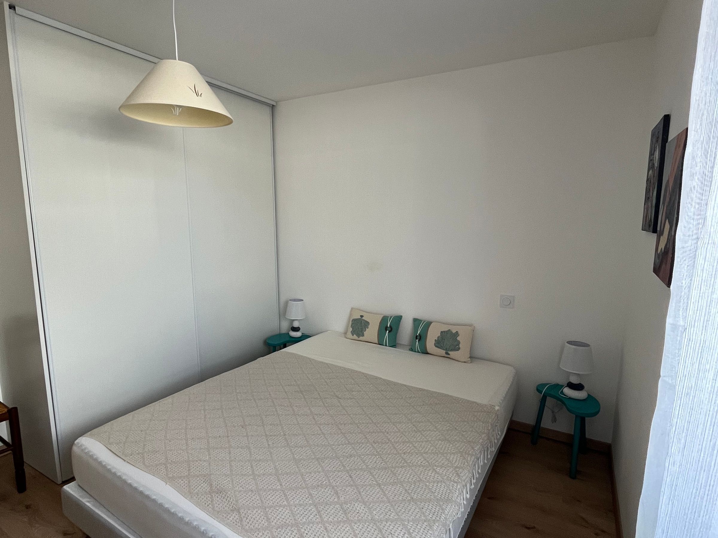 Une chambre à coucher avec un lit, deux tables de chevet, une lampe suspendue et un tableau accroché au mur.