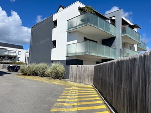 Un bâtiment moderne à plusieurs étages, doté de balcons, d’une clôture en bois et d’un chemin bordé de bandes jaunes.