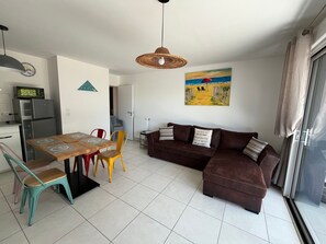 Ein Wohnbereich mit braunem Sofa, einem Esstisch mit Stühlen, einer Küche mit Kühlschrank und einem Gemälde an der Wand.