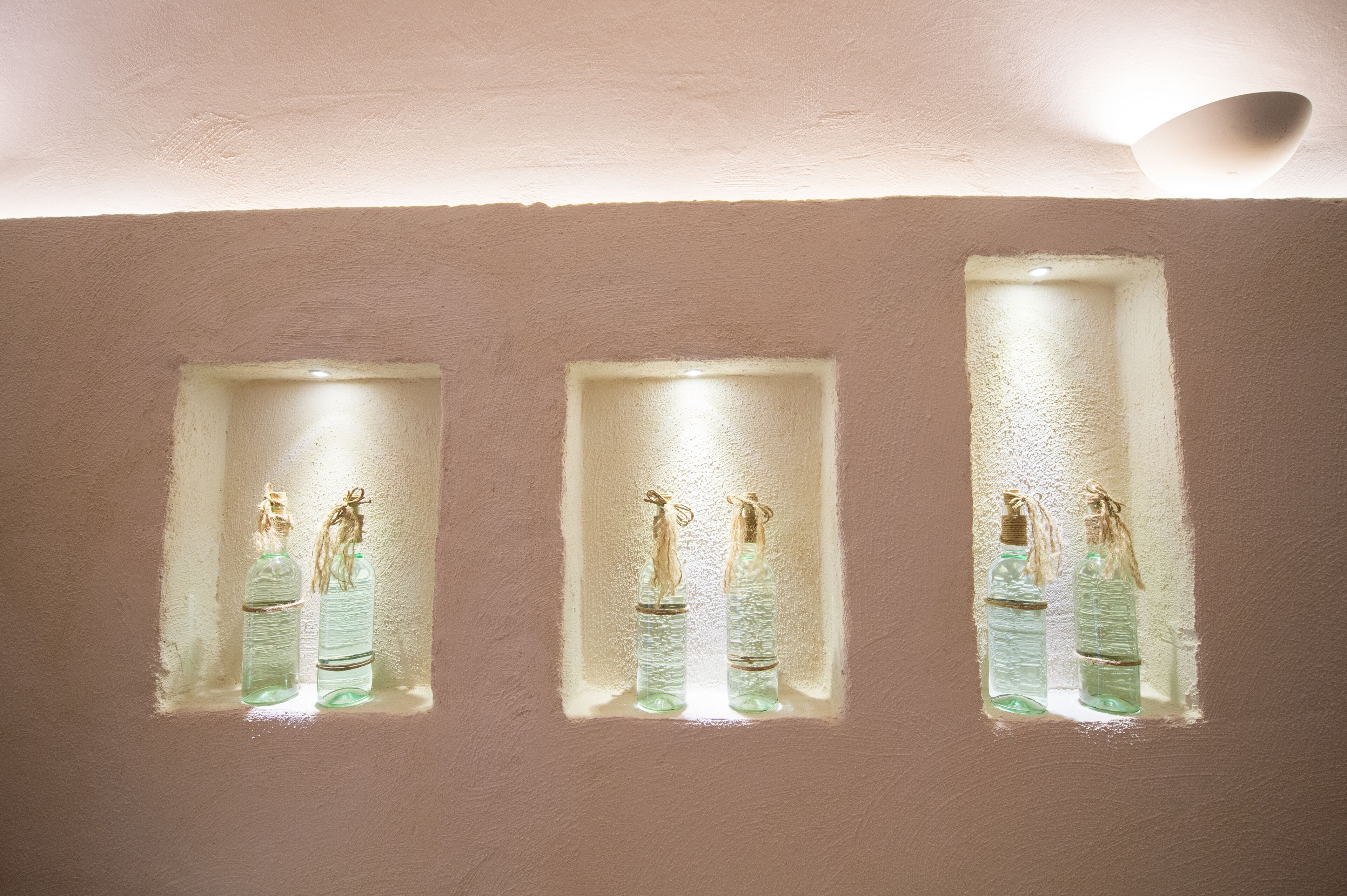 Three rectangular windows with bottles inside, against a textured wall.